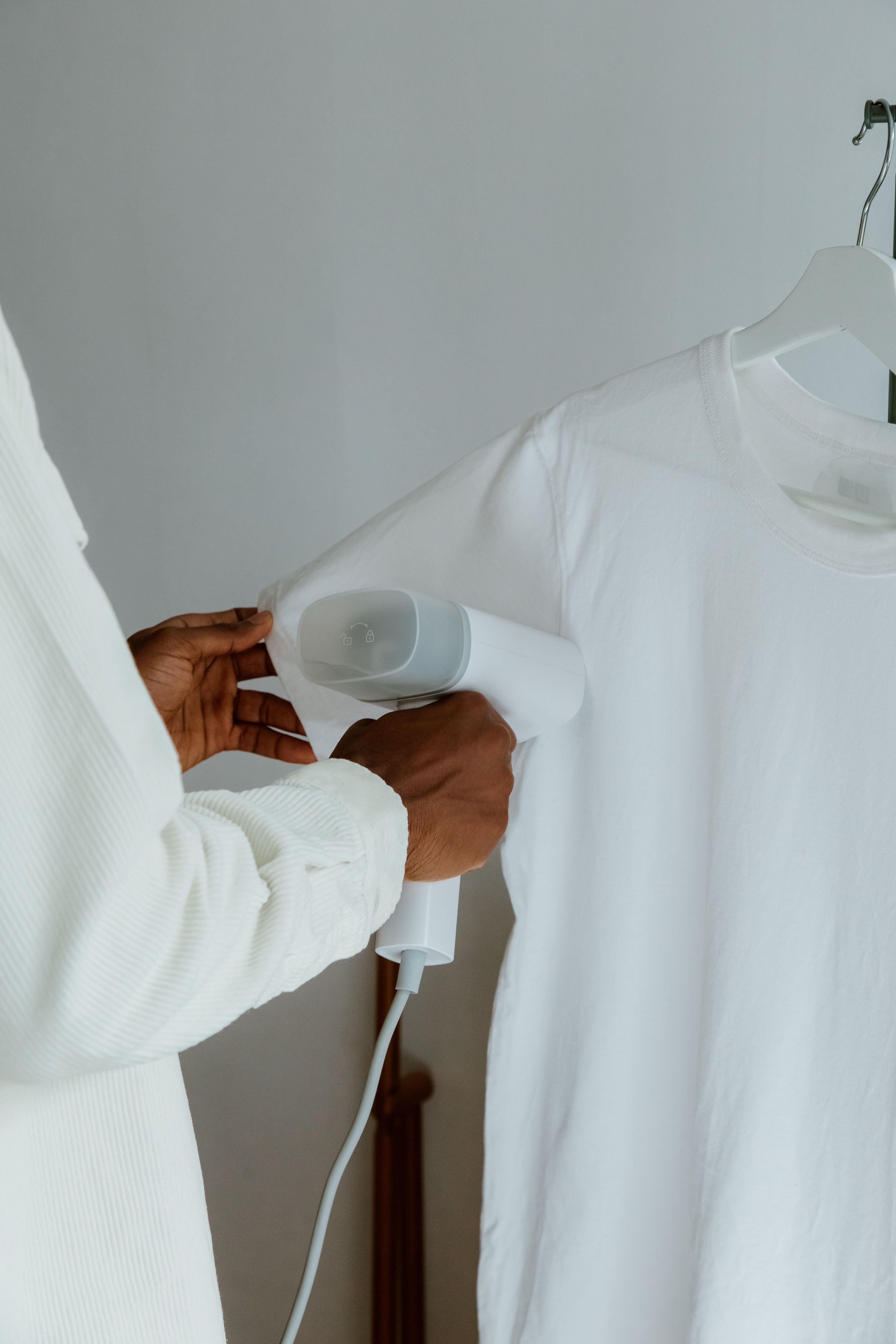 Homem passando camisa social branca pendurada em arara, usando ferro a vapor