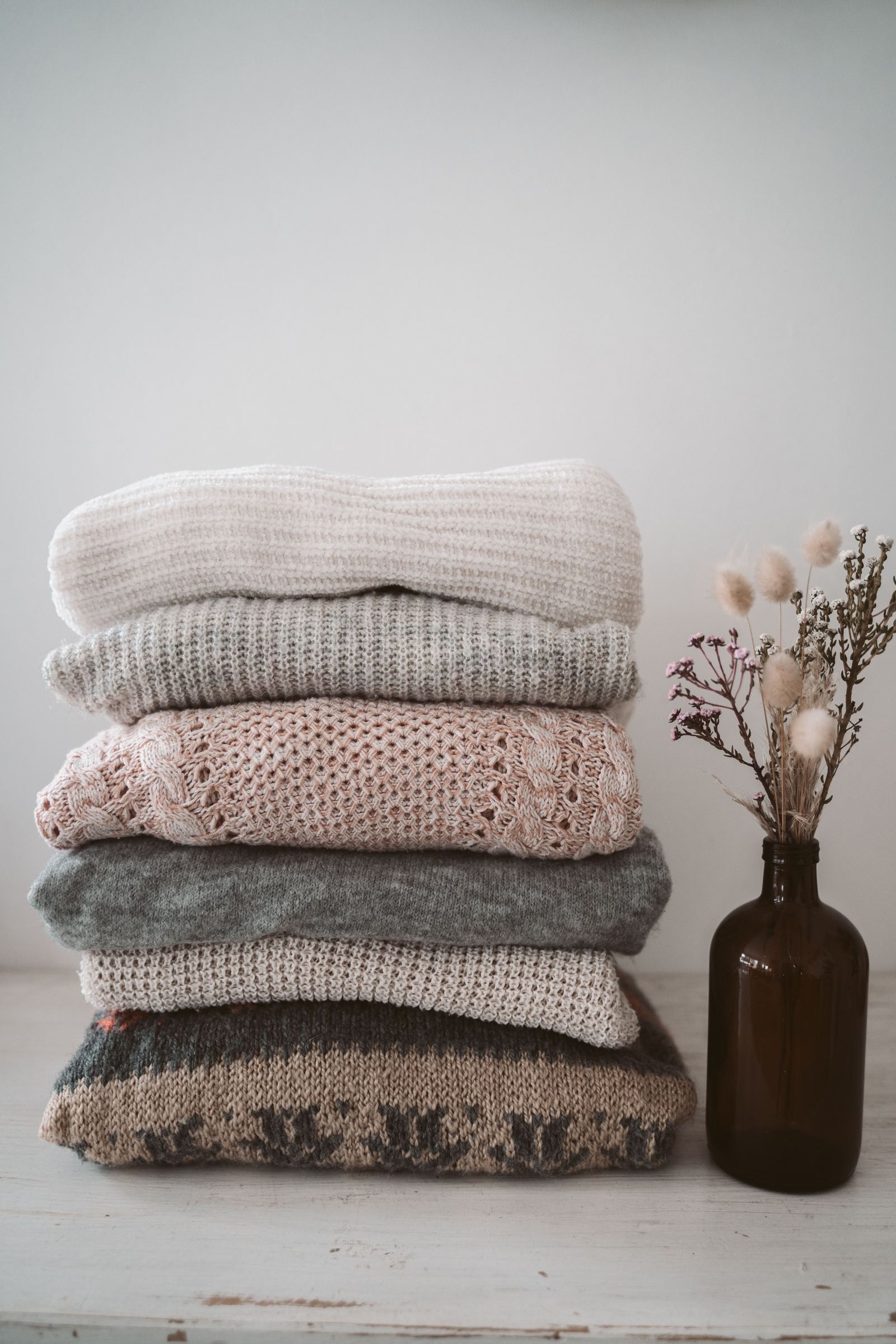 Pilha de suéteres de malha dobrados e empilhados, em tons neutros e quentes, representando peças de cashmere