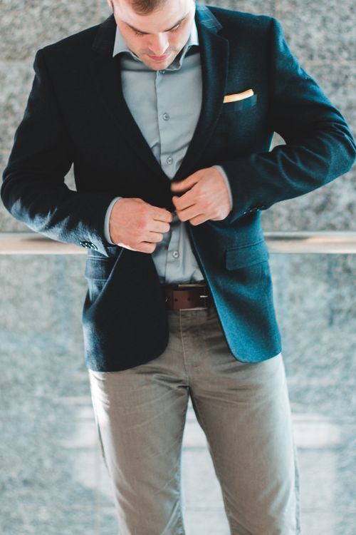 Homem elegante ajustando o blazer azul, com camisa e gravata, em ambiente interno