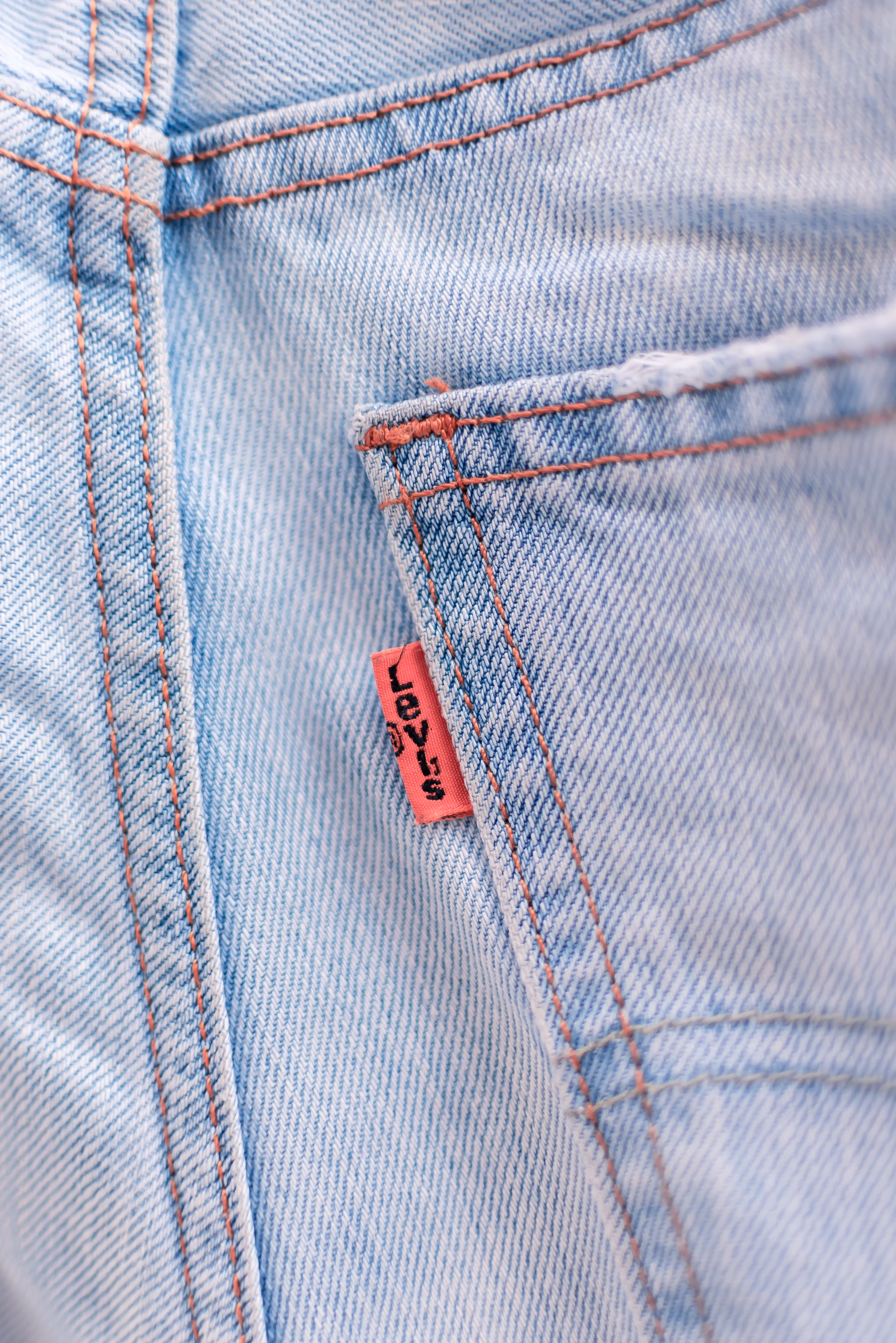 Close-up de uma calça jeans azul clara mostrando o bolso frontal, a costura reforçada e a textura característica do tecido denim