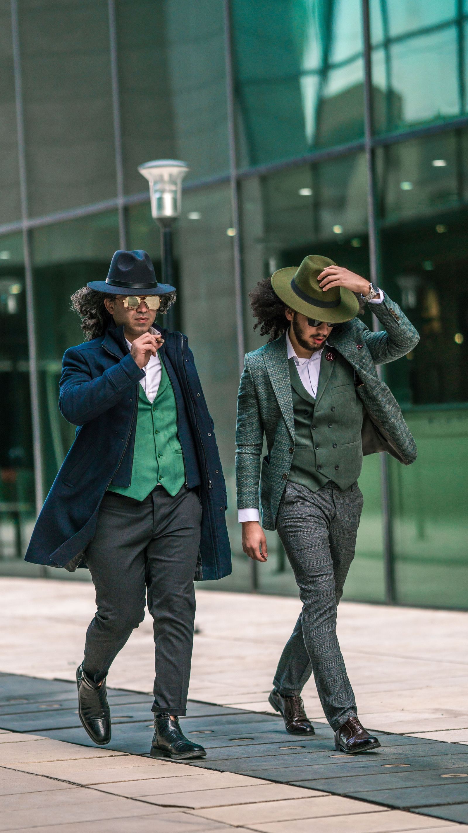 Dois homens elegantes com ternos e chapéus coloridos caminhando em ambiente urbano